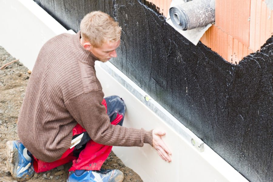 Worker installing foundation waterproofing membrane on an exterior basement wall